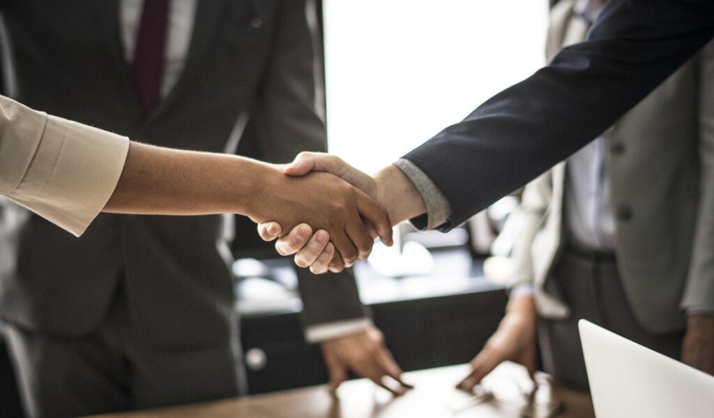 two people shaking hands while a third looks on from the background. Only the hands are visible