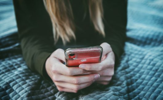 a person with long hair holds a cellphone. Although her face isn't visible, she seems to be reading something